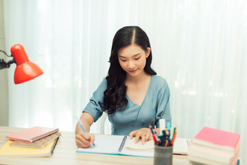 Teen girl preparing for test exam with laptop and books writing essay coursework in notebook studying at home