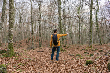 Man walking with backpack in autumn winter forest pointing hand to the trees.Hiking , travel wanderlust concept lifestyle.