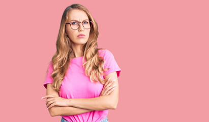 Young beautiful caucasian woman with blond hair wearing casual clothes and glasses skeptic and nervous, disapproving expression on face with crossed arms. negative person.