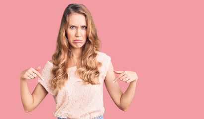 Young beautiful caucasian woman with blond hair wearing casual clothes pointing down looking sad and upset, indicating direction with fingers, unhappy and depressed.