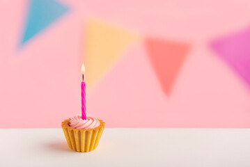 one cupcake with a candle and multi-colored flags on a white wooden surface