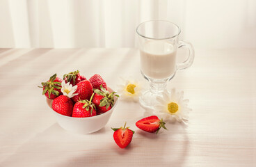 to cut strawberries, a glass of milk, chamomiles on a white wooden surface in the early morning