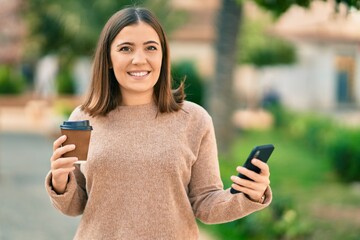 Young hispanic woman using smartphone drinking coffee at the park.
