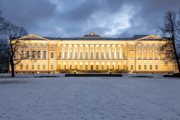 Fototapeta na wymiar A beautiful historic building with a backlit facade. Evening homestead in the park. Snowy winter evening.