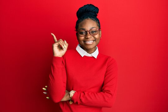 Young african american woman wearing casual clothes and glasses with a big smile on face, pointing with hand and finger to the side looking at the camera.