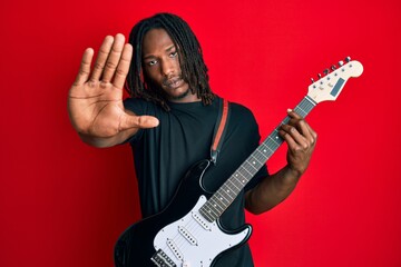 African american man with braids playing electric guitar with open hand doing stop sign with...