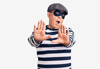 Senior handsome man wearing burglar mask and t-shirt doing stop gesture with hands palms, angry and frustration expression