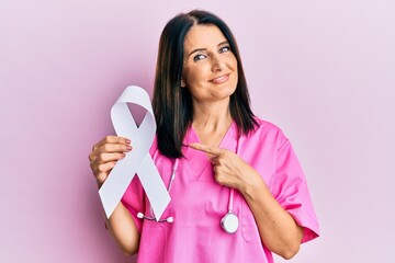Middle age brunette doctor woman holding white ribbon smiling happy pointing with hand and finger