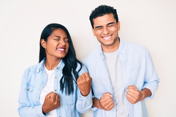 Beautiful latin young couple wearing casual clothes excited for success with arms raised and eyes...