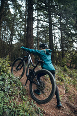 Fototapeta na wymiar Cyclist girl with mountain bike ascending mtb trail in forest
