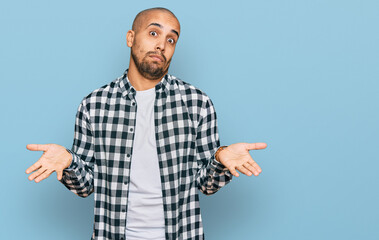 Hispanic adult man wearing casual clothes clueless and confused expression with arms and hands...