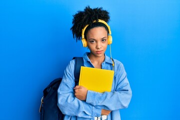 Obraz premium Young african american girl wearing student backpack and headphones holding book skeptic and nervous, frowning upset because of problem. negative person.