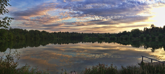 Summer landscape. Panorama of a beautiful summer sky with a reflection in the calm water of a forest lake on a warm summer evening