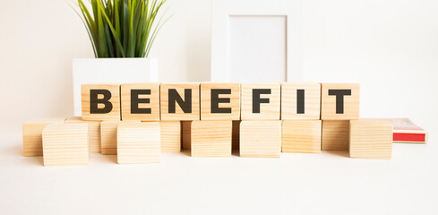 Wooden cubes with letters on a white table. The word is BENEFIT. White background.