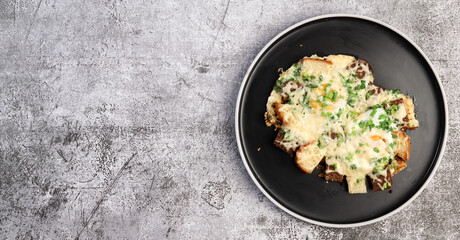 Fried eggs with bread, cheese and green onions on a round plate on a dark background. Top view, flat lay