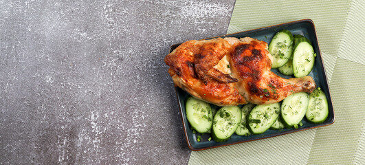 Roasted chicken on a rectangular plate on a dark background. Top view, flat lay