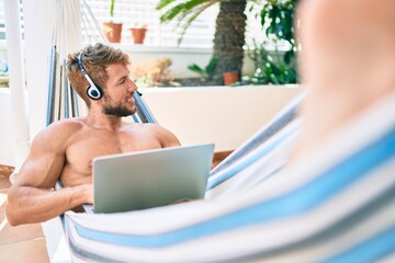 Handsome caucasian man smiling happy resting on a hammock at the terrace working from home wearing call center headset