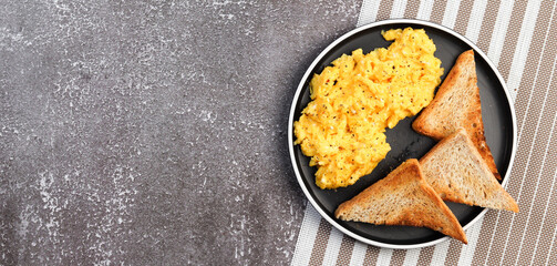 Scrambled eggs with toast on a round plate on a dark background. Top view, flat lay