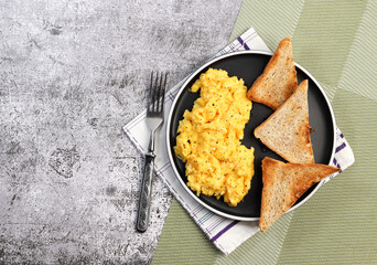Scrambled eggs with toast on a round plate on a dark background. Top view, flat lay