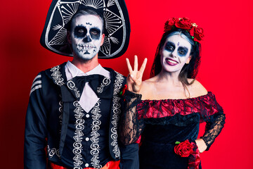 Young couple wearing mexican day of the dead costume over red showing and pointing up with fingers number three while smiling confident and happy.