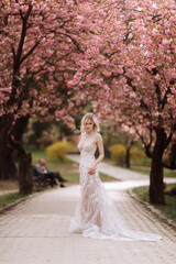 Obraz na płótnie Canvas woman's day. beautiful young woman in luxury long dress near blossoming of sakura. stylish girl near blossoming sakura flowers on background in the spring park. Harmony with nature concept