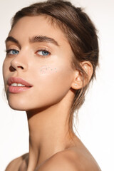 Fototapeta premium Beauty product. Caucasian girl with nude natural makeup and blue eyes, using skincare cream with collagen and argan oil for clean hydrated skin, looking sensual at camera, white background