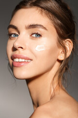 Fototapeta premium Face skin care. Woman applying cosmetic cream on clean hydrated skin portrait. Beautiful happy smiling female model with natural makeup applying facial moisturizer, beauty product. High quality