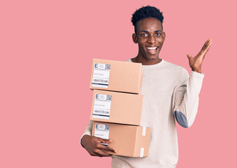 Young african american man holding delivery package celebrating victory with happy smile and winner...