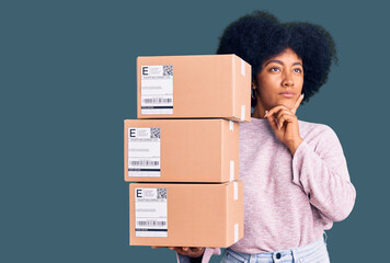 Young african american girl holding delivery package serious face thinking about question with hand...