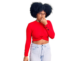 Young african american girl wearing casual clothes and glasses smelling something stinky and disgusting, intolerable smell, holding breath with fingers on nose. bad smell