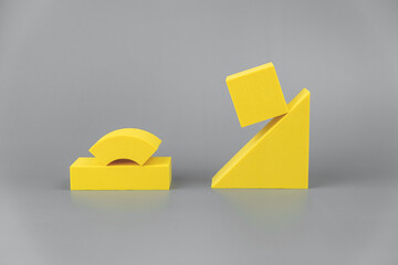 group of volumetric yellow geometric shapes on a gray background. simple shapes. the cube is hovered on one edge of the triangle