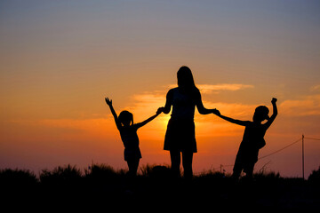 Mother and children hold hands in the background of the sunset.