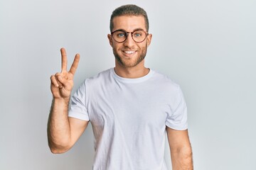 Young caucasian man wearing casual clothes and glasses showing and pointing up with fingers number two while smiling confident and happy.