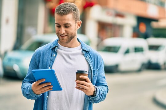 Young caucasian man smiling happy using touchpad and drinking coffee at the city.