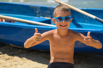 A young boy in a blue boat on the ocean. A child in sunglasses on the beach near the shore.