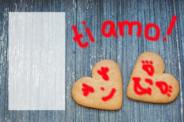 Ginger bread biscuits with fanny faces on grey wooden aged background with semi transparent copy space. Saint valentines frame with love declaration in italian. Ti amo. Invitation wallpaper. Together