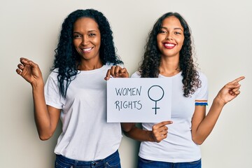 African american mother and daughter holding women rights banner smiling happy pointing with hand and finger to the side