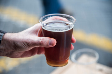 Man holding a cold glass of beer outdoors. Close up of hand holding a foaming beer in a cup. High quality photo