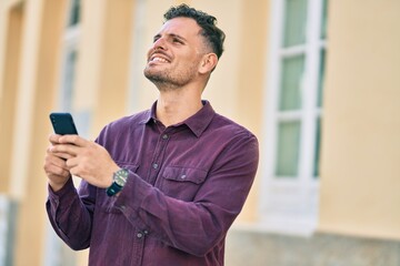 Young hispanic man smiling happy using smartphone at the city.