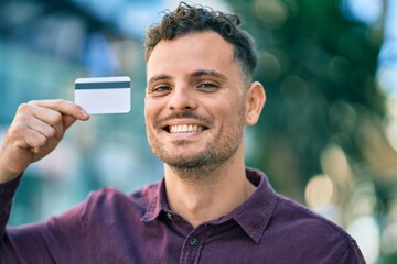 Young hispanic man smiling happy holding credit card at the city.