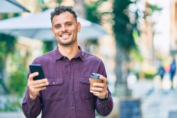 Young hispanic man using smartphone and drinking coffee at the city.