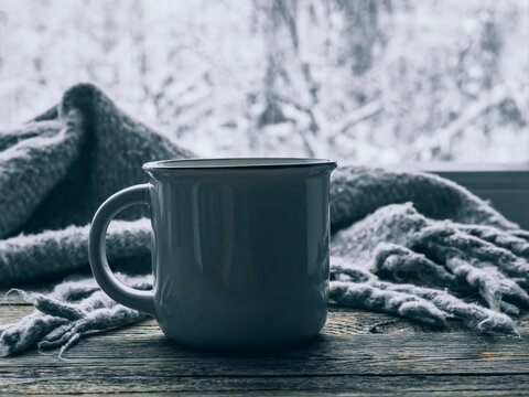 Mood, Lifestyle, Still Life Concept. Hot Cup Of Coffee And Cozy Grey Scarf On Vintage Windowsill Against Snow Landscape From Outside. Relaxing Winter Day At Home. Scandinavian Hygge Style. Soft Focus