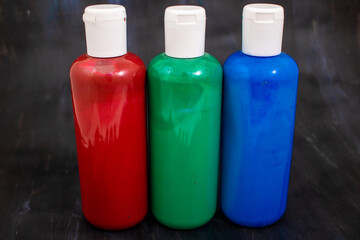Three bottles of acrylic paint in the order red, green, blue, the primary colors of the additive...