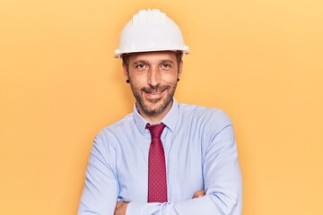 Young handsome man wearing architect hardhat happy face smiling with crossed arms looking at the camera. positive person.