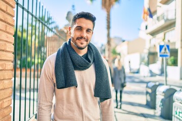 Young hispanic man smiling happy wearing scarf walking at the city.