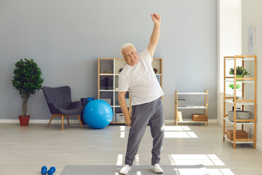 Positive mature man in home sportswear doing light exercises at home or in a rehab center.