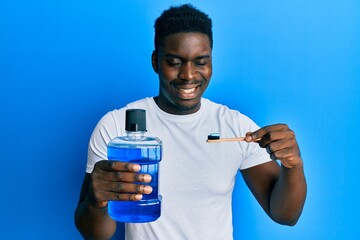 Handsome black man holding mouthwash and toothbrush for fresh breath winking looking at the camera...