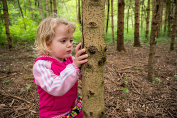 Cute blonde girl holding pine tree trunk.