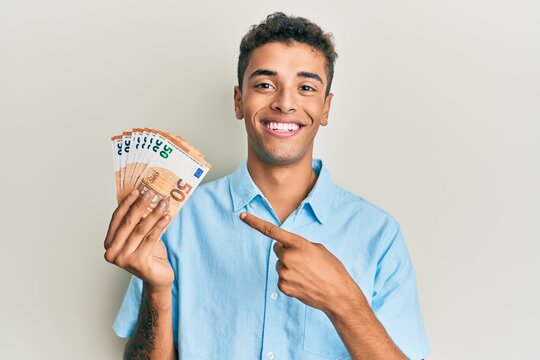 Young handsome african american man holding bunch of 50 euro banknotes smiling happy pointing with hand and finger
