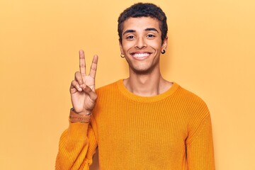 Young african amercian man wearing casual clothes smiling with happy face winking at the camera doing victory sign. number two.